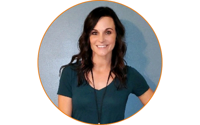 A woman with long, dark hair is smiling while standing against a blue wall. She is wearing a dark green t-shirt and a lanyard, embodying the spirit of the Career Support Lab that offers weekly career help.